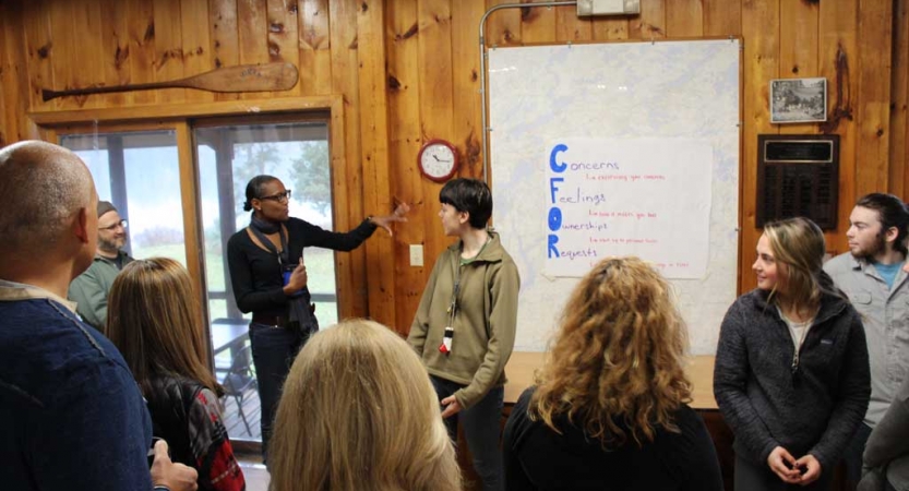 A person points at a whiteboard in front of a group of people during the family seminar of an outward bound intercept course.